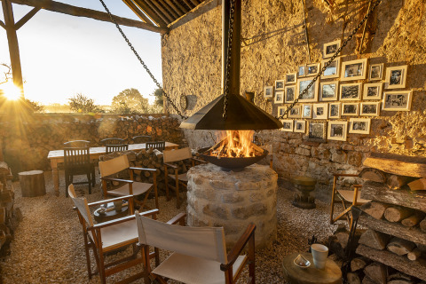 Zona exterior en Kimaro Farmhouse - Safaritenten Bourgogne con chimenea, sillas de madera y muro de piedra.