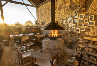 Outdoor lounge at Kimaro Farmhouse - Safaritenten Bourgogne with firepit, wooden chairs, stone wall and woodpile.