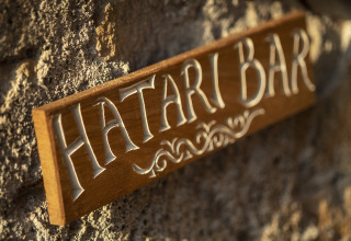 Cartel de madera con la inscripción 'Hatari Bar' en una pared de piedra en Kimaro Farmhouse - Safaritenten Bourgogne.