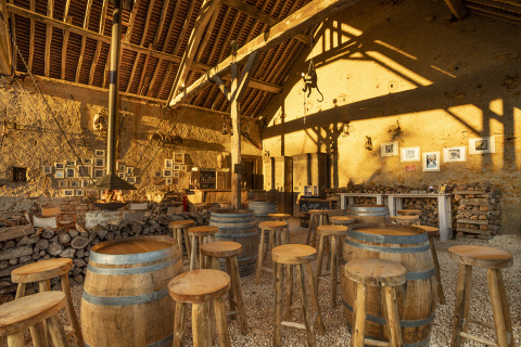 Bar rústico con barriles de madera, taburetes y luz cálida en Kimaro Farmhouse, glamping en Borgoña.