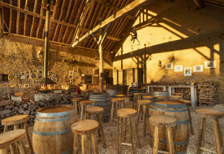 Bar rústico con barriles de madera, taburetes y luz cálida en Kimaro Farmhouse, glamping en Borgoña.