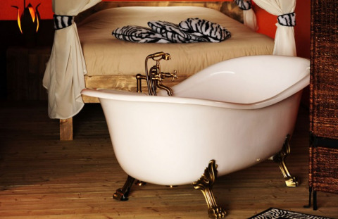 Bañera independiente de patas doradas junto a una cama en tienda de glamping en Kimaro Farmhouse, Borgoña.