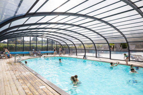 Piscina coperta con tetto trasparente e ospiti che si divertono a Huttopia Les Falaises - Glamping Normandië.