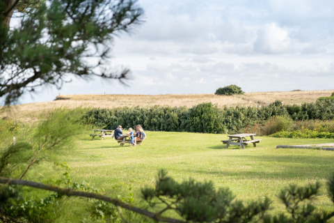 Familia disfrutando un picnic en una mesa de campo verde en Huttopia Les Falaises Glamping Normandië, entorno rural.