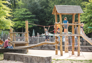 Children playing on a wooden playground set among trees at Huttopia Les Falaises - Glamping Normandië.