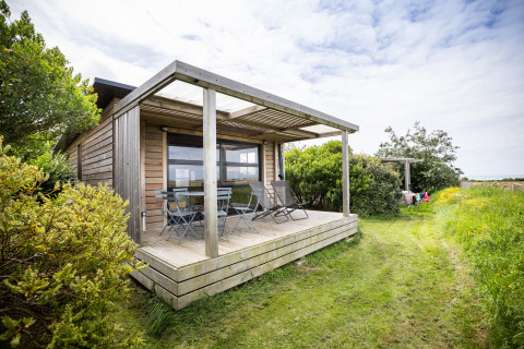 Glamping accommodatie in houten chalet bij Huttopia Les Falaises, Normandië, omgeven door natuur en groen.