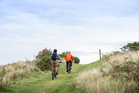 Twee mensen fietsen over een groene route bij Huttopia Les Falaises - Glamping Normandië, genieten van de natuur.