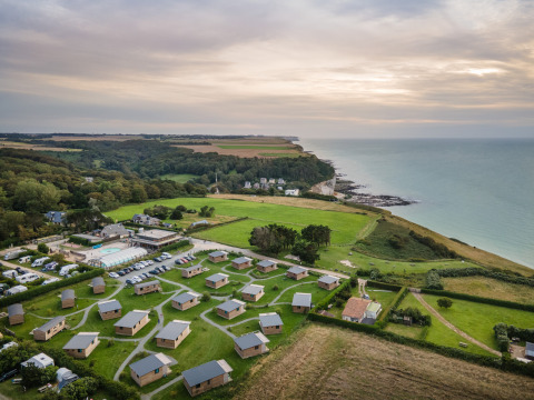 Vista aerea del glamping Huttopia Les Falaises in Normandia, con bungalow, prati verdi e scogliera sul mare.