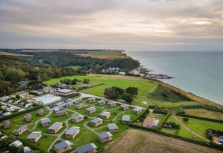 Luftfoto af glampingpladsen Huttopia Les Falaises i Normandiet med hytter, marker og udsigt over havet.