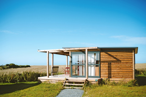 Moderne glampingaccommodatie bij Huttopia Les Falaises in Normandië, met houten gevel en uitzicht op veld.