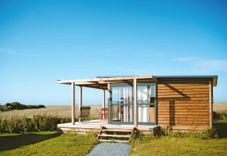 Cabane de glamping moderne à Huttopia Les Falaises en Normandie, avec terrasse et vue sur la campagne.