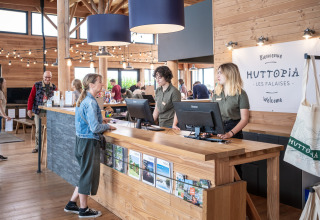 Receptionen ved Huttopia Les Falaises Glamping i Normandiet med gæster og personale i en hyggelig stemning.
