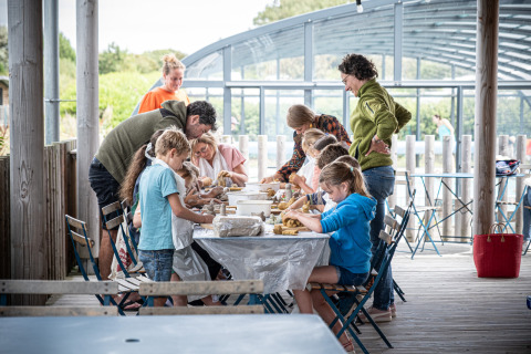 Kinder und Erwachsene töpfern gemeinsam bei Huttopia Les Falaises - Glamping Normandie unter einer Überdachung.