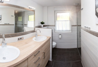 Modernes Badezimmer mit Doppelwaschbecken, Toilette und Dusche im Glampingbereich von Camping Teichmann.