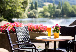 Zona de asientos al aire libre con sillas de mimbre, flores y cerveza junto al lago en Glamping Teichmann.