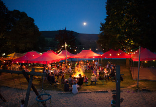 Noche de fogata y personas bajo carpas iluminadas en Camping en Vakantiepark Teichmann - Glamping Hessen.