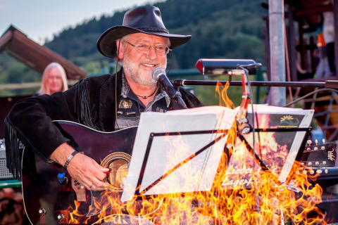 En musiker iført cowboyhat spiller guitar ved et bål under en koncert i Camping en Vakantiepark Teichmann.