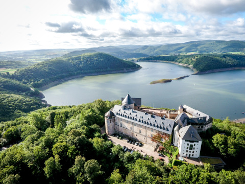 Aerial view of a lakeside castle nestled in green hills, perfect for glamping at Camping Teichmann in Hessen.