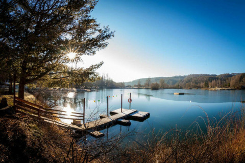 Sonniger See mit Steg, Bäumen und ruhiger Umgebung bei Camping en Vakantiepark Teichmann - Glamping Hessen.