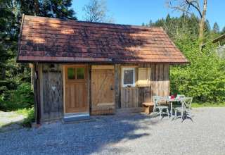 Charming wooden glamping cabin with a red tiled roof and outdoor seating in Baden-Württemberg countryside.