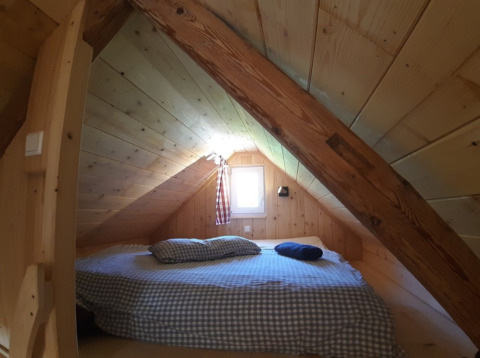 Cozy sleeping loft with wooden walls and beams in a rustic cabin, perfect for countryside glamping.