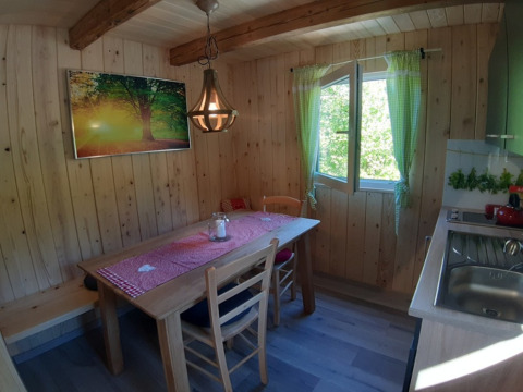 Gemütliche Holzhütte mit Essbereich, Holzdecke, grün karierten Vorhängen und Sonnenlicht.