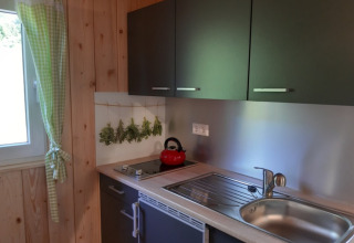 Kleine kitchenette met groene kasten, hangende kruiden en raam in Gallushof - Boshut op het platteland, Baden-Württemberg.