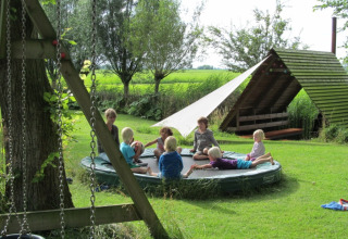Børn og voksne hygger sig omkring en trampolin i en grøn glamping-lejr hos It Dreamlân Ecolodges Friesland.