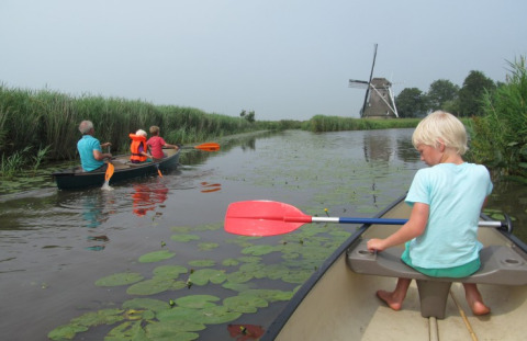 Famiglia in canoa su un canale con ninfee a It Dreamlân - Ecolodges Friesland, mulino a vento sullo sfondo.