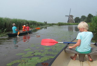Family canoeing on a lily pad-filled canal at It Dreamlân - Ecolodges Friesland with windmill in the background.
