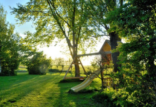 Sonniger Garten mit Baumhaus und Rutsche bei It Dreamlân - Ecolodges Friesland Glamping Unterkunft.