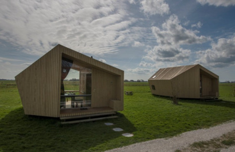 Due moderni ecolodge in legno su un prato verde sotto un cielo nuvoloso a It Dreamlân - Ecolodges Friesland.