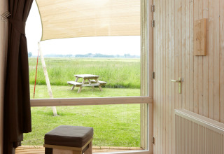 Blick aus einer Glamping-Unterkunft bei It Dreamlân Ecolodges Friesland auf eine grüne Wiese mit Picknicktisch.