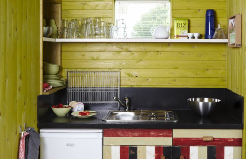Piccola cucina presso It Dreamlân Ecolodges Friesland, con mobili colorati, pareti in legno e scaffali.