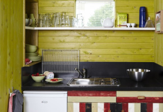 Compact kitchen at It Dreamlân Ecolodges Friesland with colorful cabinets, wooden walls, and open shelving.