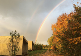 Glamping presso It Dreamlân - Ecolodges Friesland con lodge moderni, colori autunnali e arcobaleno nel cielo.