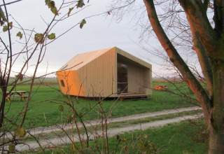 Ecolodge in legno per glamping a It Dreamlân - Ecolodges Friesland, immersa in un campo verde e naturale.