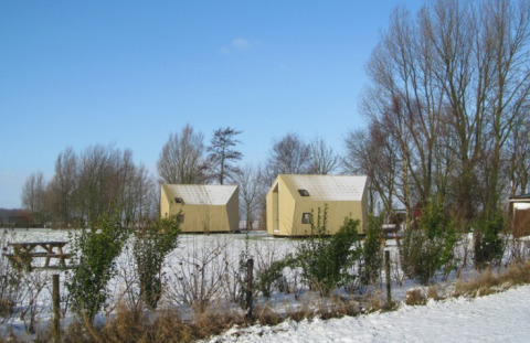 Ecolodges bij It Dreamlân in Friesland in de winter, omgeven door kale bomen en een besneeuwd veld.