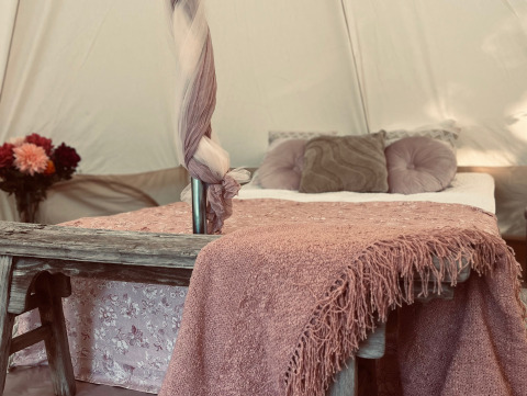 Gezellige glamping accommodatie in West-Vlaanderen met comfortabel bed, roze plaid en verse bloemen.