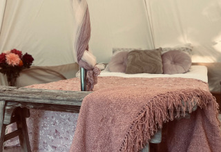 Alojamiento glamping acogedor en West-Vlaanderen con cama cómoda, manta rosa y decoración floral.