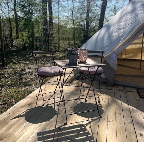 Udendørs træterrasse med bord og stole foran et glampingtelt hos Glamping Goed Van Den Bogaerde.