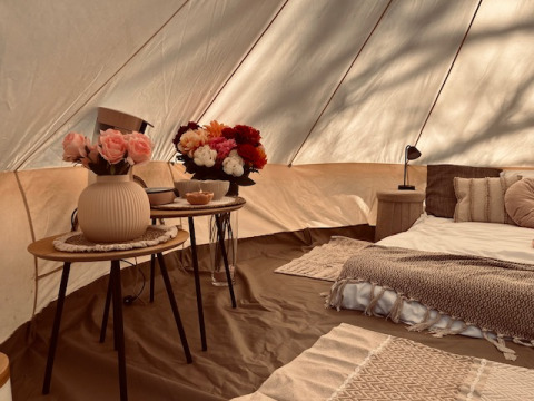 Interior de glamping de lujo en Glamping Goed Van Den Bogaerde con cama cómoda, decoración floral y ambiente acogedor.