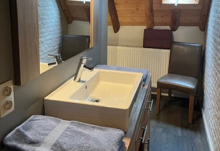 Modern bathroom at Glamping Goed Van Den Bogaerde with towels, sink, wooden beams, and a windowed loft ceiling.