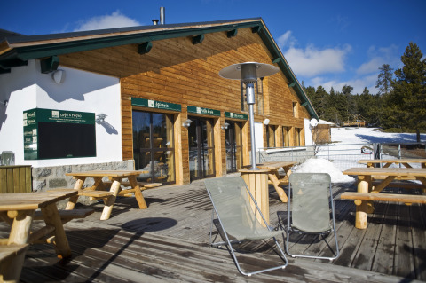 Udendørs terrasse ved Huttopia Winter Chalets – Font Romeu med træborde, stole og sne i Pyrenæerne.