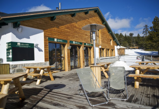 Terraza exterior en Huttopia Winter Chalets – Font Romeu con mesas de madera, sillas y nieve en los Pirineos.