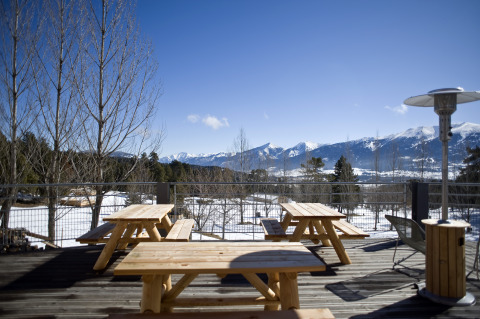 Terrasse mit Holzbänken und Panoramablick auf verschneite Berge bei Huttopia Winter Chalets, Pyrenäen.