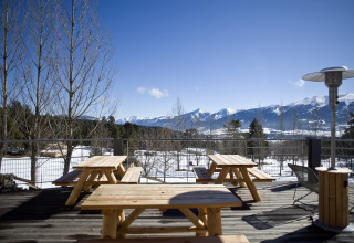 Outdoor terrace with wooden benches and a scenic view of snowy mountains at Huttopia Winter Chalets, Pyrenees.