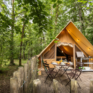 Sistemazione glamping nella natura con tenda accogliente e area pranzo esterna al Village Huttopia Lanmary-Périgord.