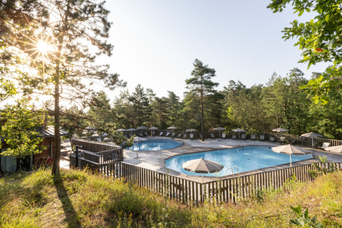 Außenpool mit Sonnenschirmen und Liegen, umgeben von Wald bei Village Huttopia Lanmary-Périgord Glamping Dordogne.