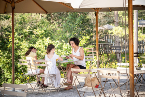 Family enjoying breakfast outdoors under umbrellas at Village Huttopia Lanmary-Périgord glamping site.
